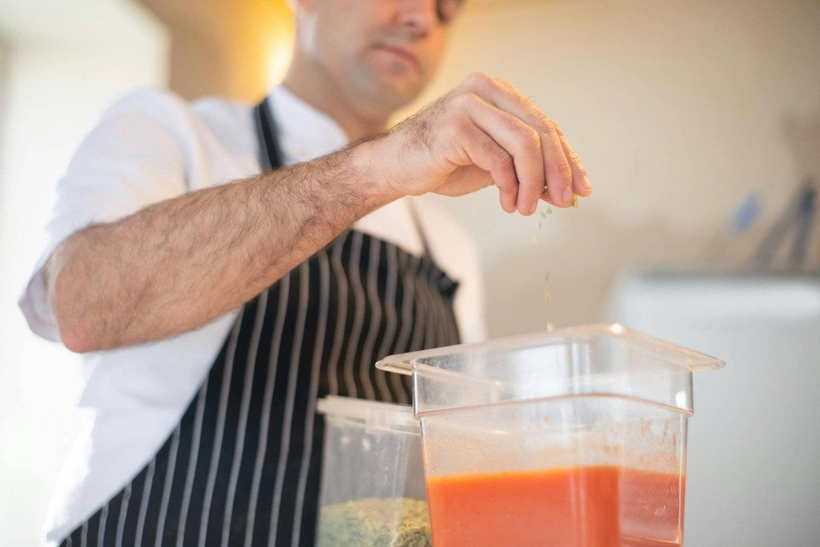 Chef in Portugal skillfully seasons tomato sauce in a modern kitchen setting.