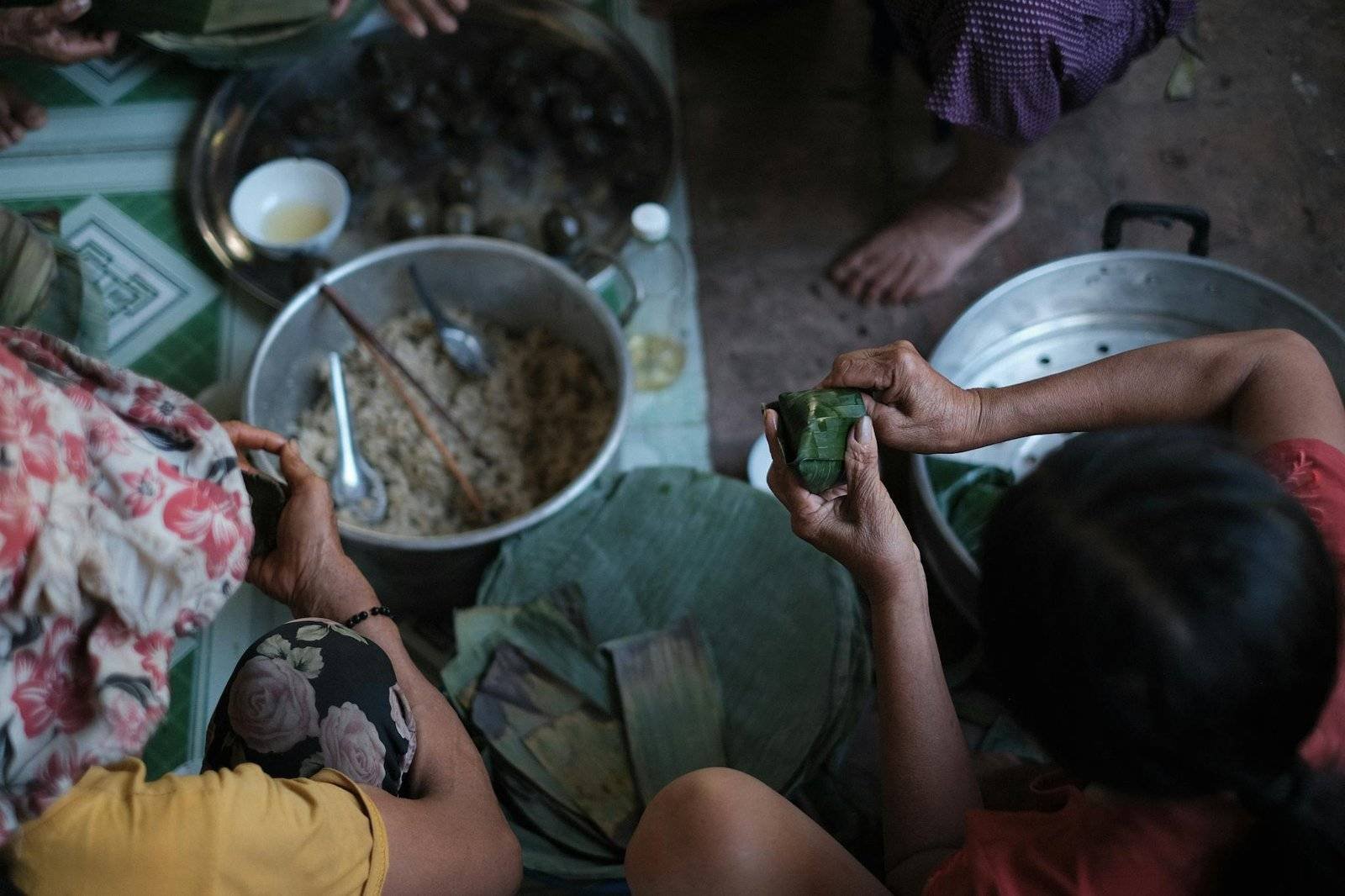 People preparing traditional food using banana leaves in a rural Vietnamese kitchen.